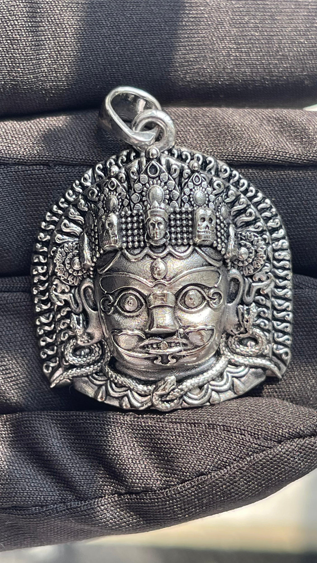 A hand holding the silver Kaal Bhairav pendant to show its size, scale, and the quality of the sterling silver material.